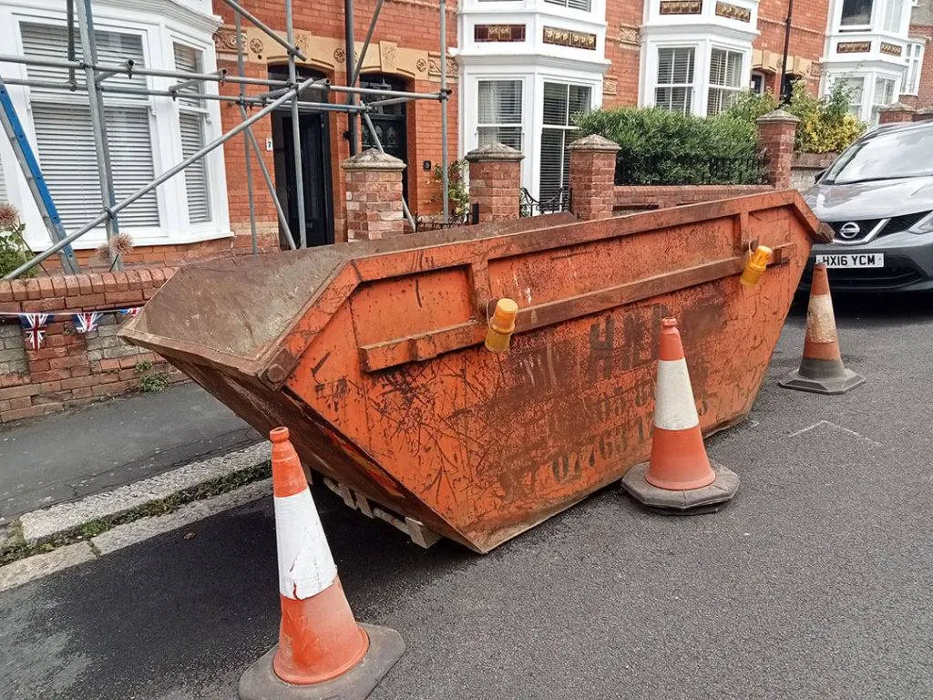 A rusted skip sitting on the side of a road.